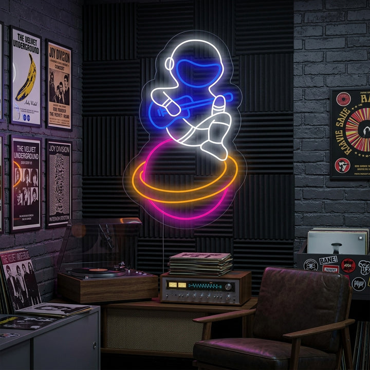 A neon sign showing a musician astronaut playing guitar while sitting on a planet, glowing blue and yellow against a modern room background.