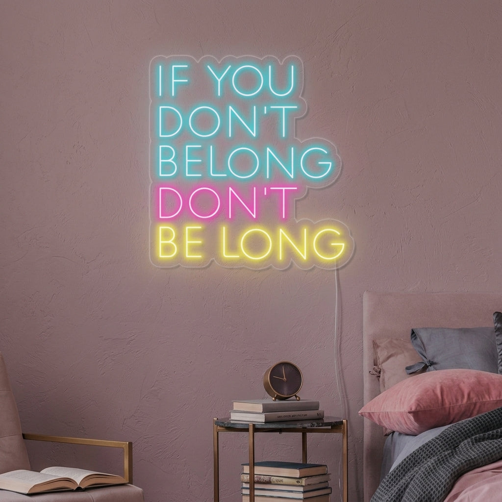 A vibrant yellow neon sign glowing above a grey couch in a cozy living room, displaying the text 'If You Dont Belong Dont Be Long'.