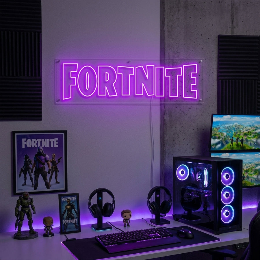 Fortnite neon sign glowing blue on a dark wall above a gaming desk setup in a dimly lit room.