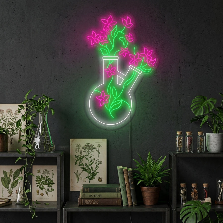A glowing blue and green neon sign depicting a chemistry beaker used as a vase with a small plant, mounted on a modern concrete wall with plants below.