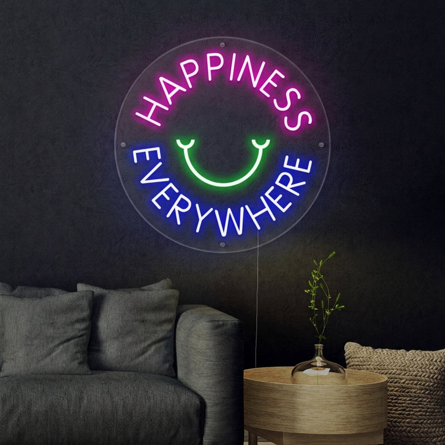 A lifestyle photo of the 'Happyness Everywhere' glowing script neon sign mounted on a brick wall above a cozy armchair.