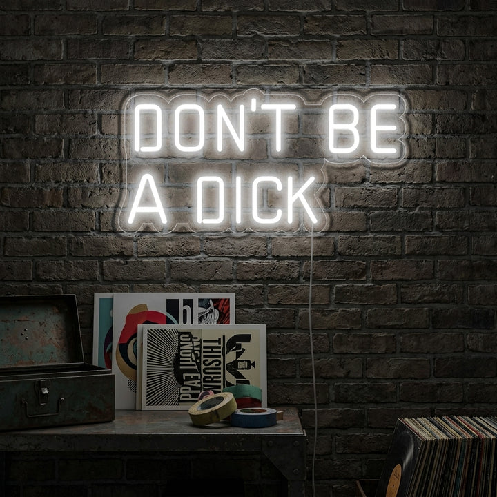 A glowing blue 'Dont Be a Dick' handwritten-style neon sign hangs on a dark brick wall in a modern living room setting.
