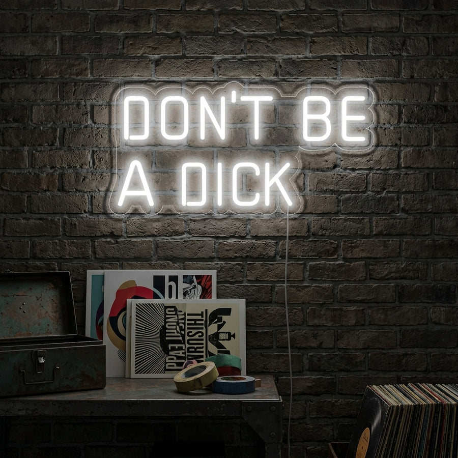 A glowing blue 'Dont Be a Dick' handwritten-style neon sign hangs on a dark brick wall in a modern living room setting.