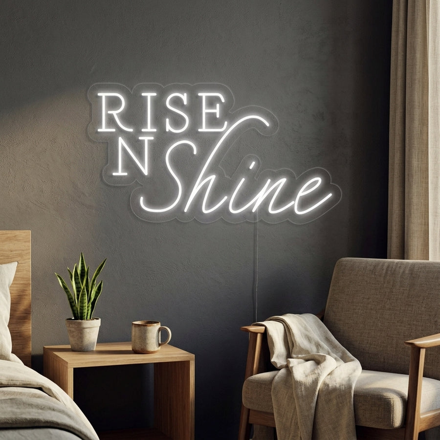 Warm glowing 'Rise N Shine' neon sign in script font, mounted on a wall above a kitchen counter or breakfast bar, integrated into a natural home setting.