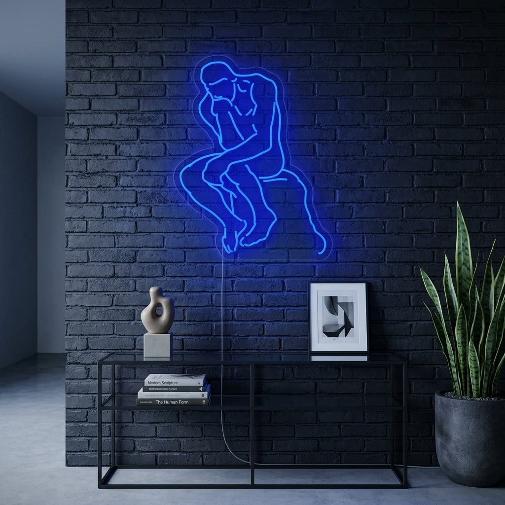 A wall-mounted neon sign depicting the classic Rodin sculpture 'The Thinker' in a thoughtful pose, casting a strong red glow in a dimly lit, contemporary living space.