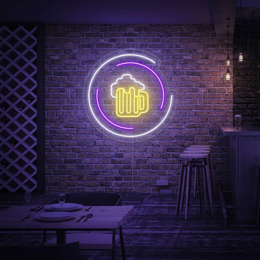 A glowing yellow neon sign in the shape of a foaming beer mug, displayed on a textured dark wall in a dimly lit bar setting with blurred seating and bottles in the background.