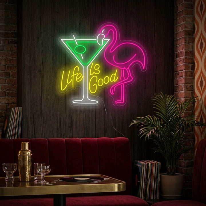 Life Is Good cocktail neon sign glowing above a home bar setup next to a plant.