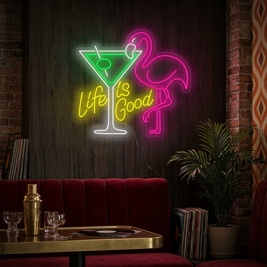Life Is Good cocktail neon sign glowing above a home bar setup next to a plant.