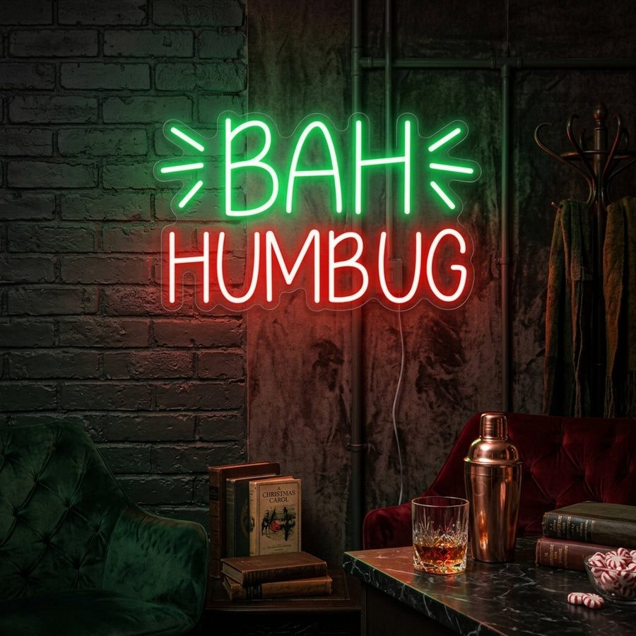 A glowing 'Bah Humbug' neon sign in cursive script mounted on a dark brick wall above a cozy armchair with a festive plaid blanket.