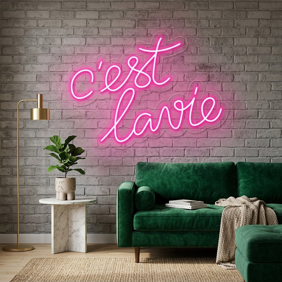 A "Cest lavie" neon sign glowing on a textured apartment wall above a cozy seating area.