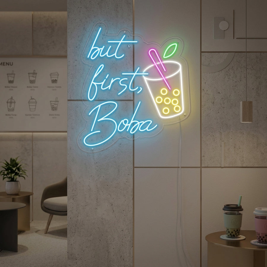 A vibrant 'But First Boba' neon sign glowing brightly on a wall in a trendy cafe setting.