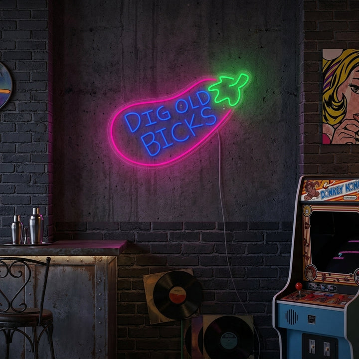A lifestyle photograph showing the glowing 'Big Old Bicks Eggplant' neon sign displayed on a brick wall in a modern living room setting.