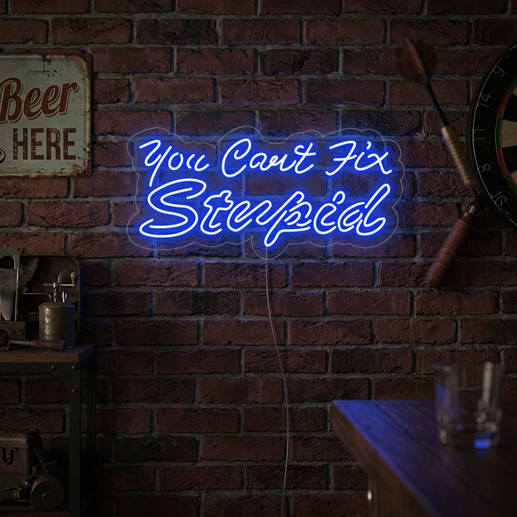 A candid lifestyle photo shows the lighted 'You Can't Fix Stupid' neon sign hanging above a rustic wooden workbench in a dimly lit garage or man cave, casting a warm orange glow. Tools are organized beneath it.