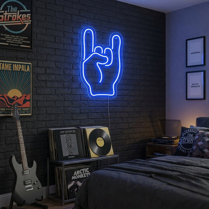 A hand forming the rock on sign illuminated in vibrant neon, glowing brightly on a brick wall in a lifestyle setting.