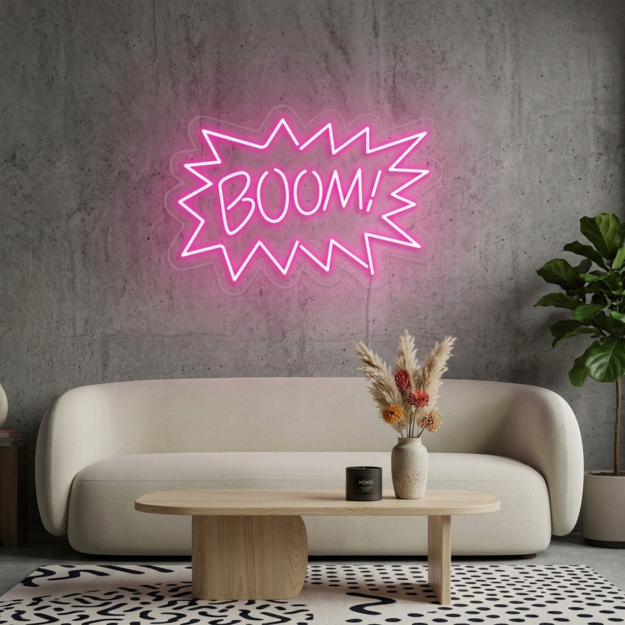 A vibrant 'Boom' text neon sign glowing in bright pink, yellow, and red colors, mounted on a textured brick wall above a cozy seating area in a modern living room.