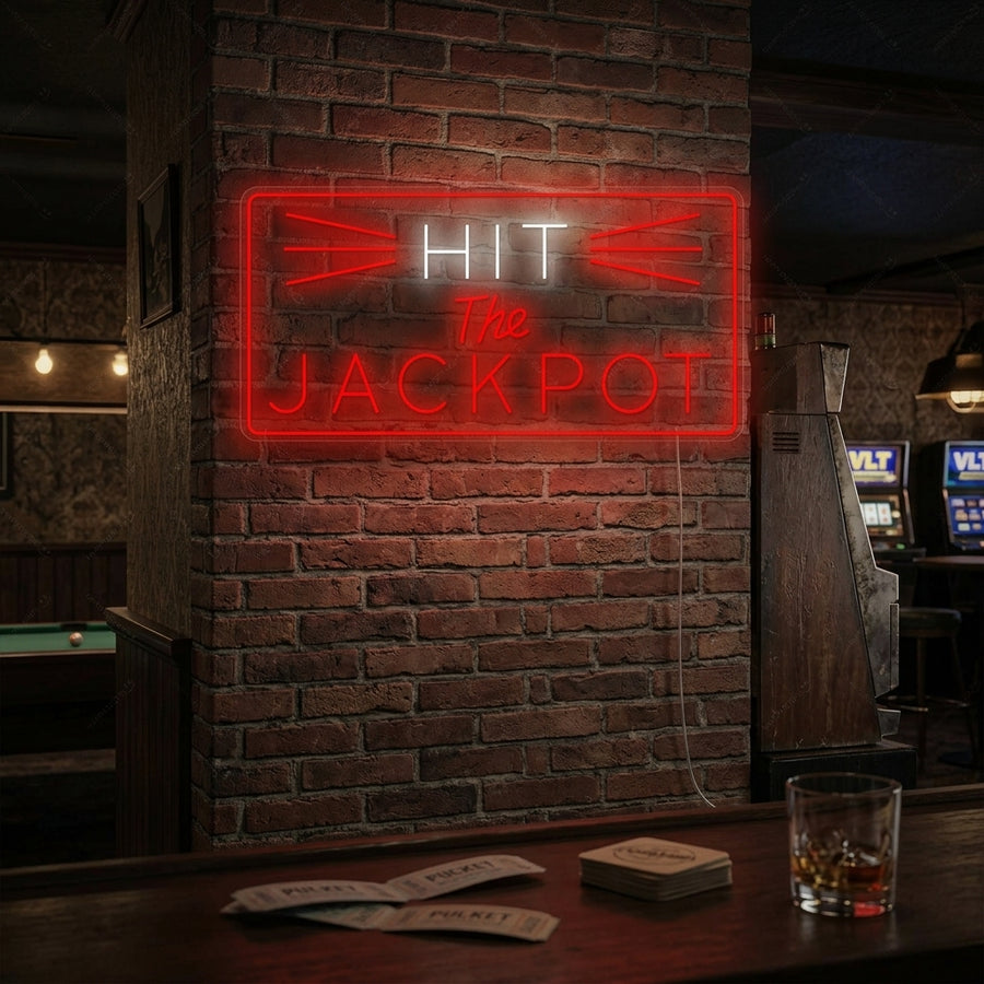 A vibrant red 'Hit The Jackpot' neon sign glows brightly against a dark brick wall in a lifestyle setting, illuminating a glass of whiskey and poker chips on a table below.