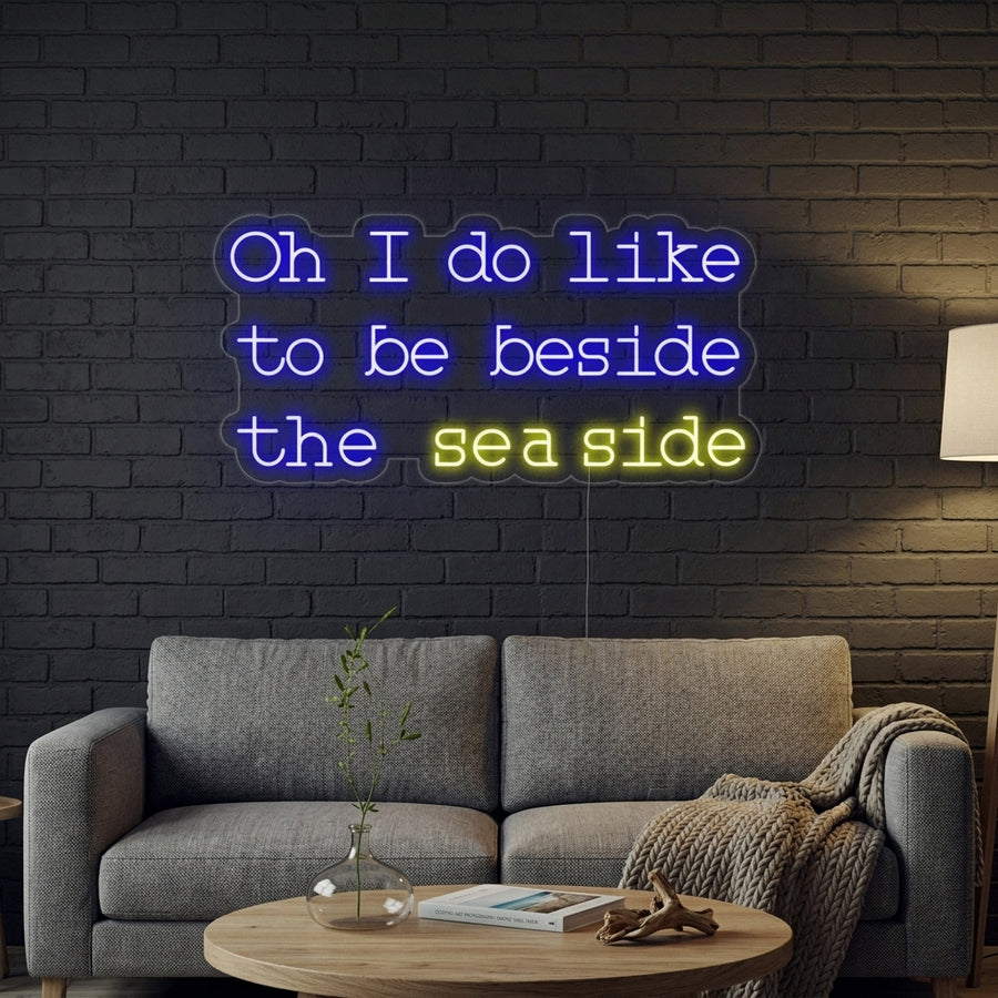 An illuminated 'Oh I do like to be beside the seaside' neon sign mounted on a textured wall in a bright, modern living room.