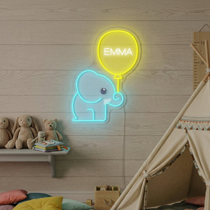 Customizable neon sign featuring a charming blue elephant holding a pink balloon, glowing warmly above a toy shelf in a kids' room.