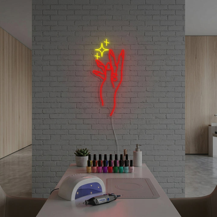 A glowing neon sign featuring a hand with long, painted red nails and white geometric outlines is mounted on a textured grey wall in a brightly lit nail salon setting.