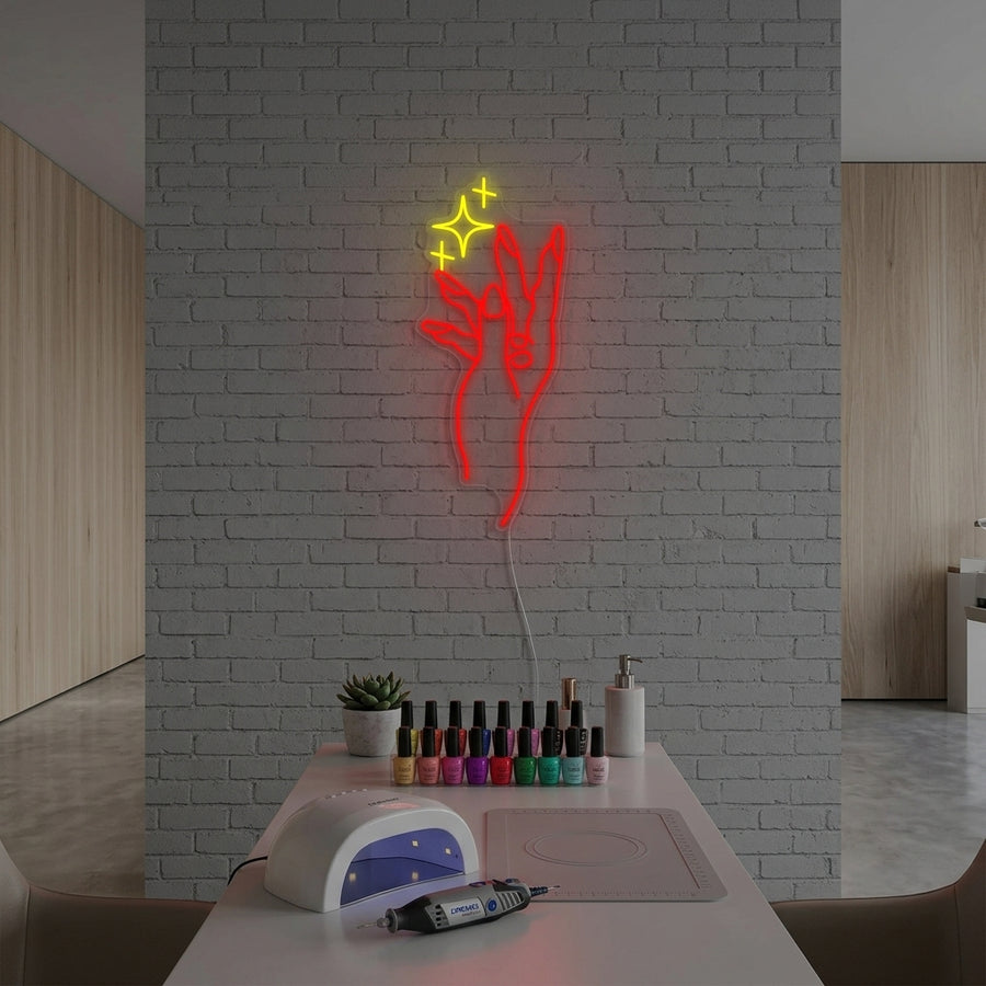 A glowing neon sign featuring a hand with long, painted red nails and white geometric outlines is mounted on a textured grey wall in a brightly lit nail salon setting.
