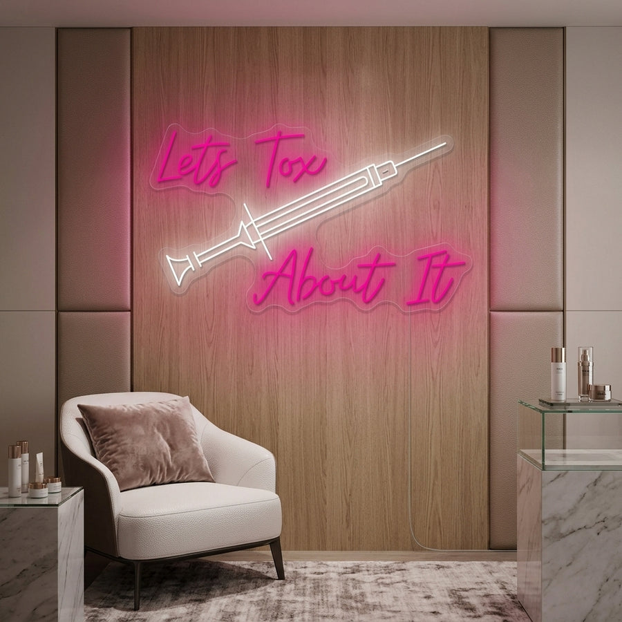 A glowing blue 'Lets Tox About It' neon sign in a scripted font, displayed above a soft pink velvet sofa in a modern waiting area.