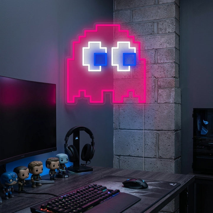 A vibrant arcade ghost neon sign glowing blue on a dark brick wall in a well-decorated gaming room setup.