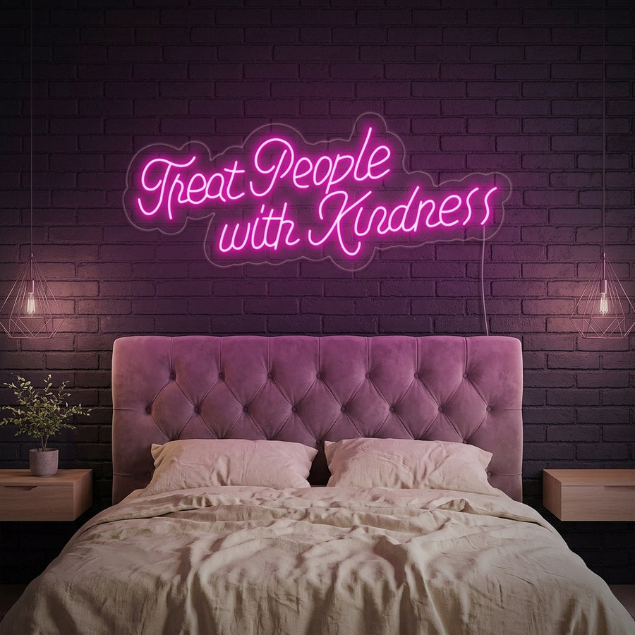 A vibrant Treat People With Kindness neon sign in glowing pink cursive, mounted on a wall above a modern desk setup in a stylish home office.