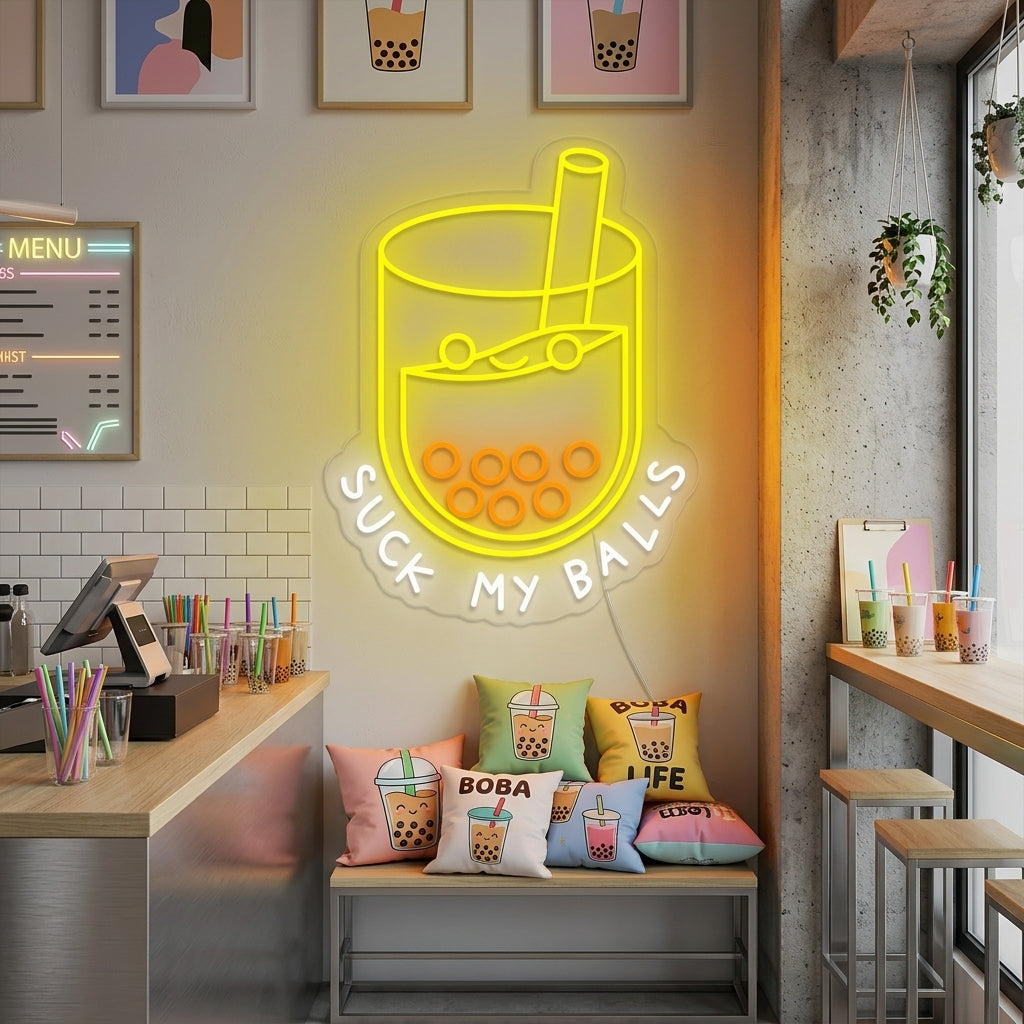 Cheeky "Suck my balls" boba tea neon sign glowing vibrant pink and orange with a cartoon bubble tea graphic on a dark textured brick wall in a cozy shop setting.