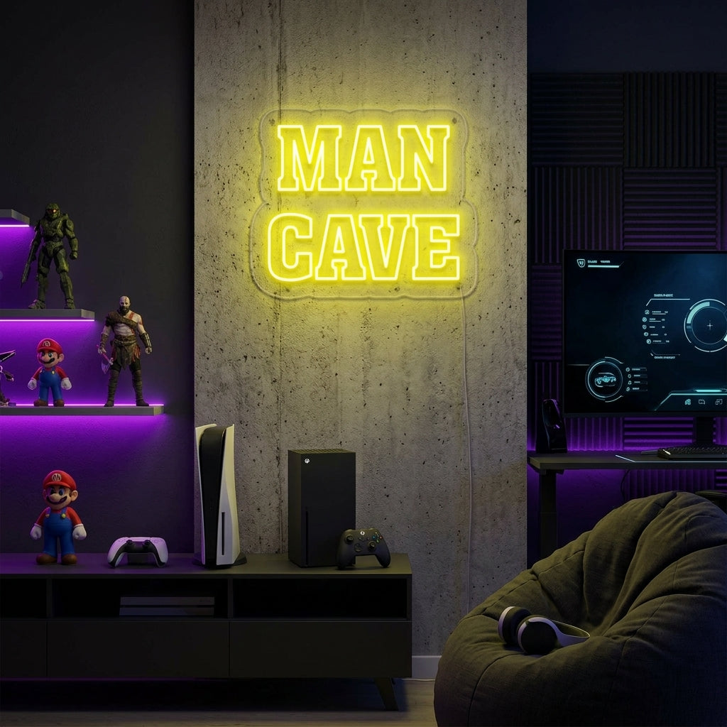 A vibrant neon sign with blue text reading 'MAN CAVE' below a warm white game controller outline, mounted in a dark, stylized gaming room setup with multiple monitors and LED lights.