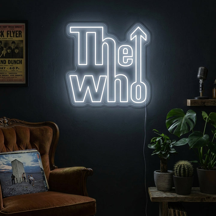 A lifestyle shot of 'The Who' neon sign lit up and hanging on a brick wall in a cozy room above vintage rock posters.