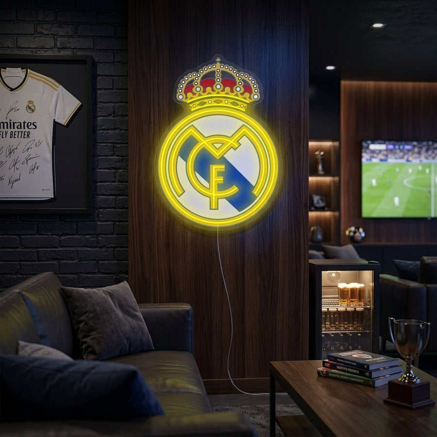 A vibrant Real Madrid club crest neon sign glowing brightly on a textured grey wall in a modern living room setting.