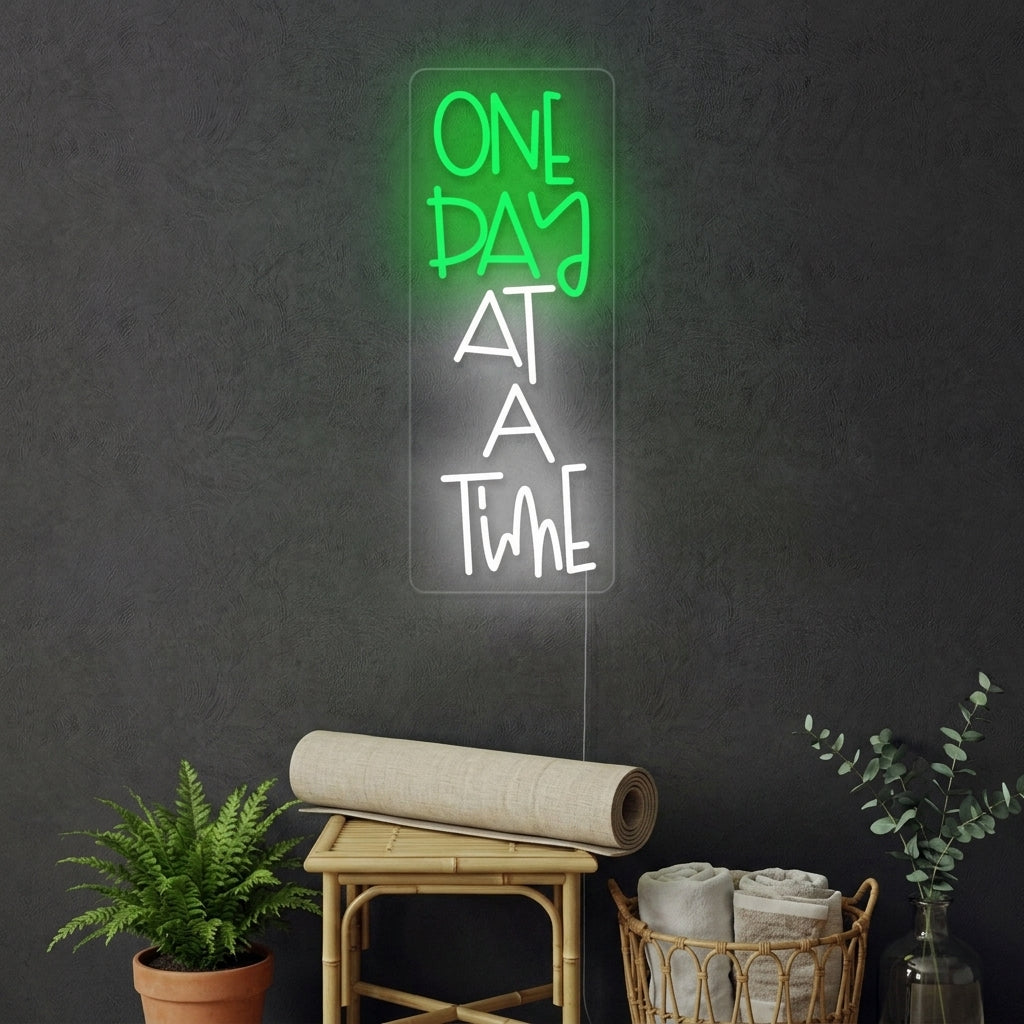 A lifestyle photograph of the illuminated "One Day At A Time" neon sign mounted on a stylish interior wall.