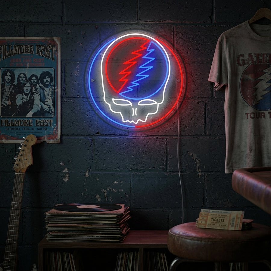 A glowing Grateful Dead neon sign featuring a blue skull with a lightning bolt on the forehead, mounted on a dark wall in a cozy room setting.