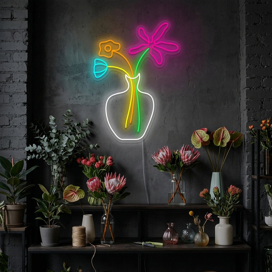 A glowing pink flower neon sign mounted on a dark textured bedroom wall above a wooden bedside table.