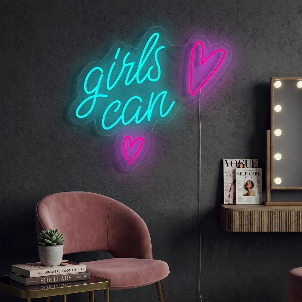 A close-up photograph of the 'Girls Can' neon sign glowing in bright pink against a textured wall, with a small potted plant sitting on a wooden surface below it in a modern home decor setting.
