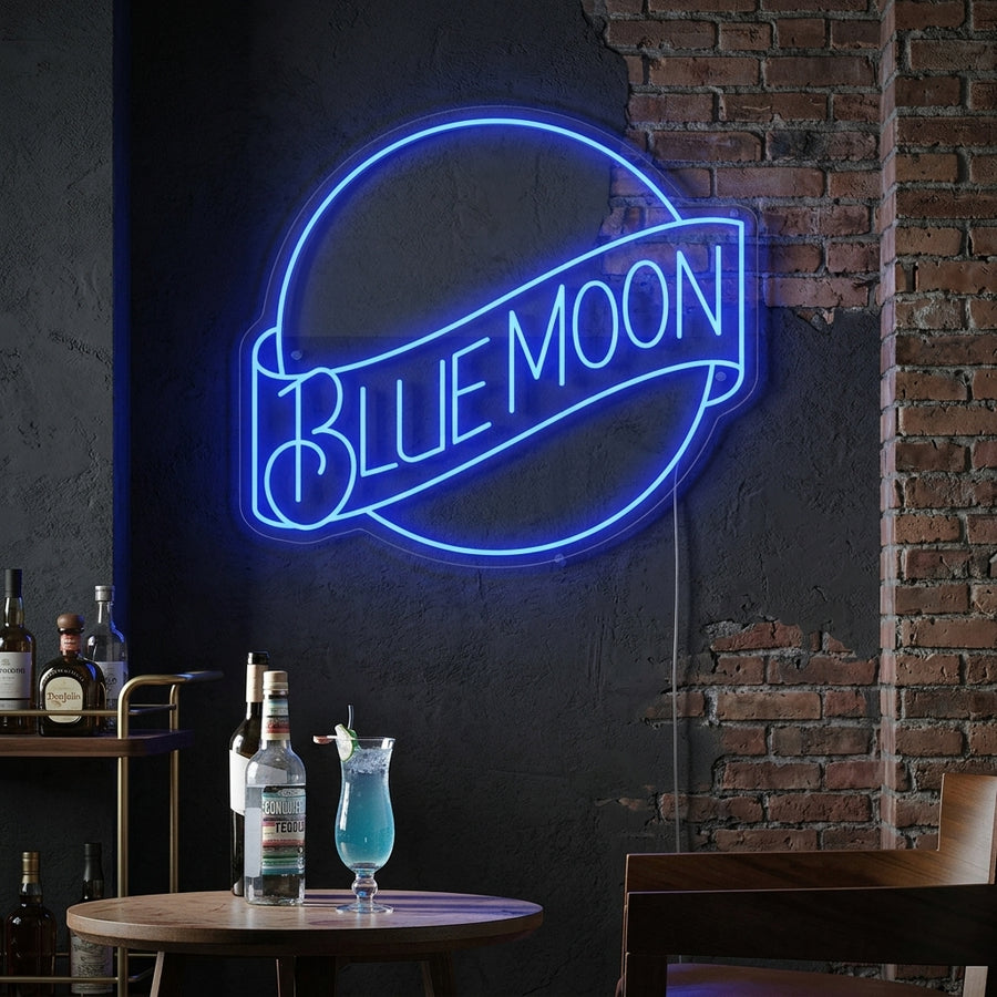 Glowing blue and white Blue Moon Lager Beer neon sign with crescent moon logo and orange peel accent, mounted above a wooden bar cart with glasses.
