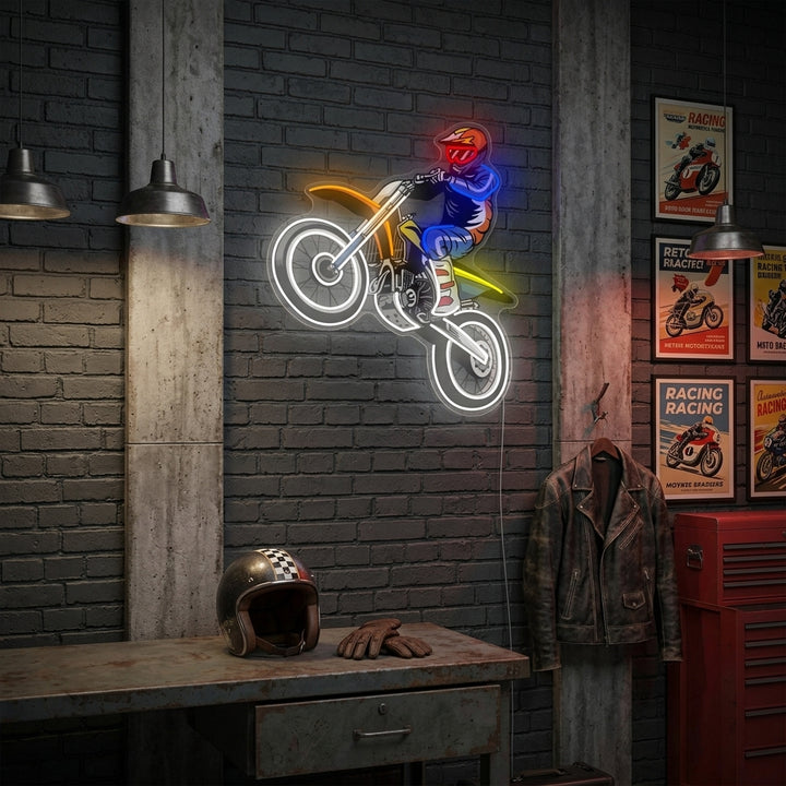 A glowing blue and orange neon sign of a motocross rider jumping, mounted on a rustic wood plank wall above a workshop bench with tools.