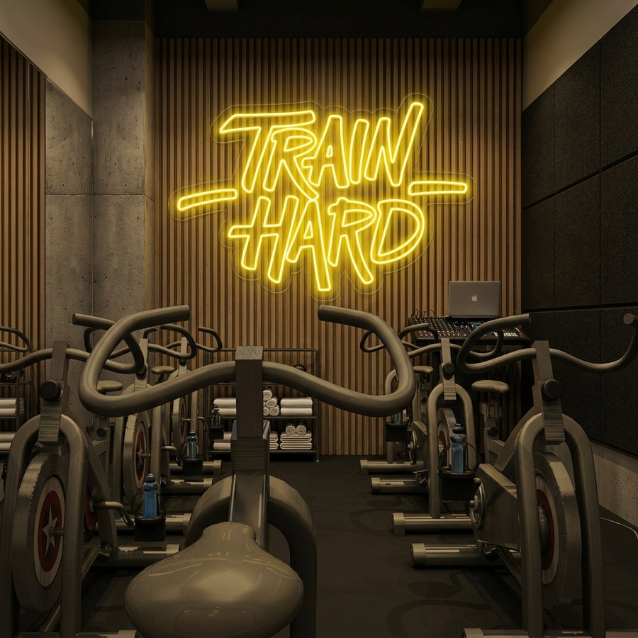 Vibrant blue 'Train Hard' neon sign mounted on a textured dark gym wall above dumbbells and resistance bands.
