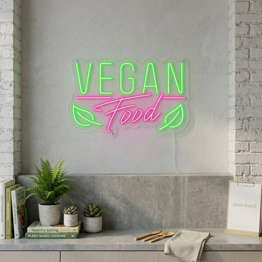 A vibrant 'Vegan Food' neon sign with glowing script is displayed in a cozy cafe window, surrounded by plants and outdoor patio seating in the background.
