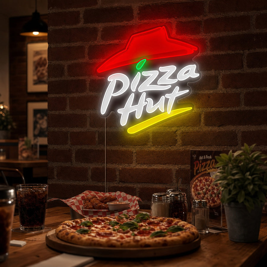 A person relaxing in a room at night with a glowing Pizza Hut logo neon sign mounted on the wall above the sofa.