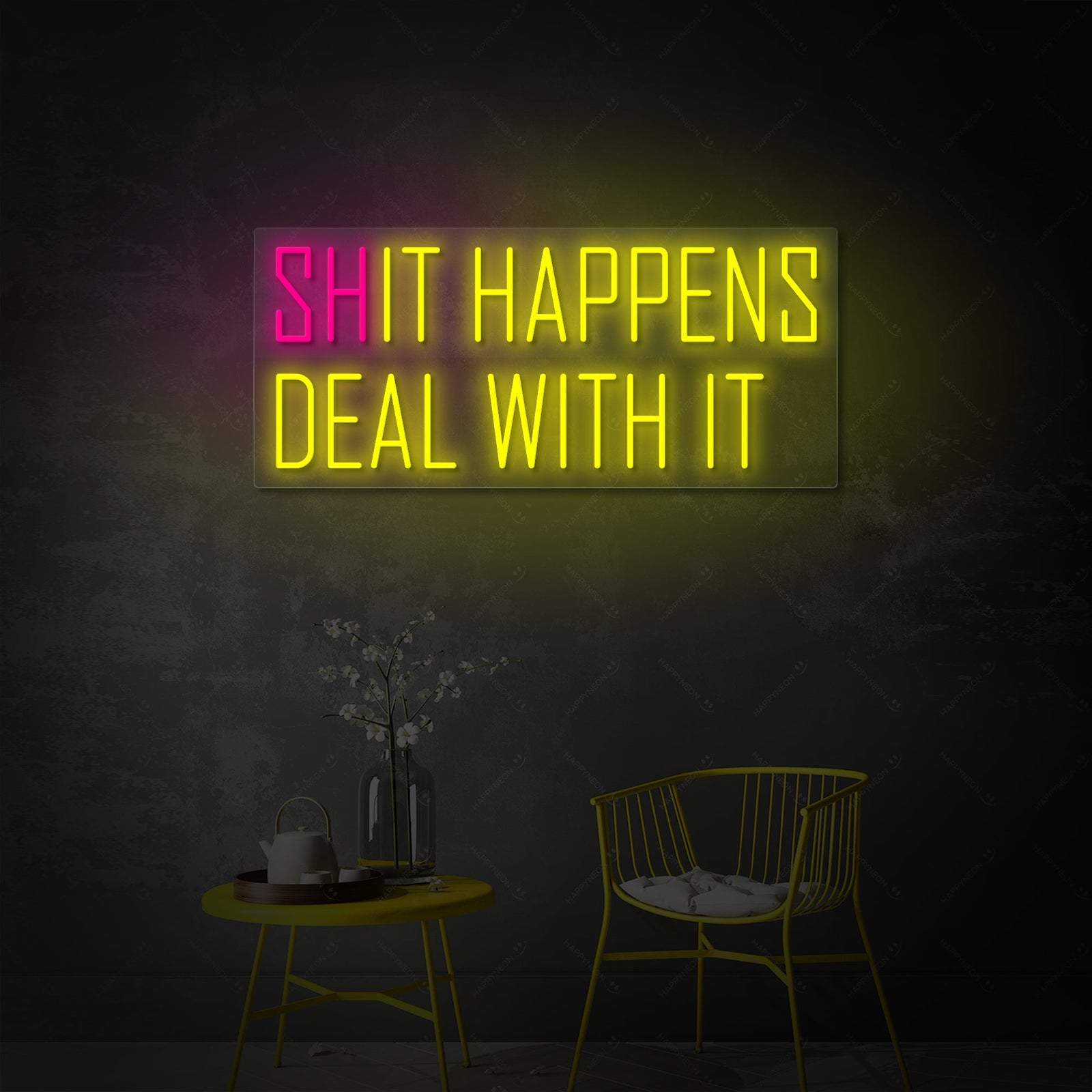 A brightly glowing 'Shit happens It happens' neon sign is clearly visible against a slightly textured, modern industrial concrete wall background, casting a soft light below.
