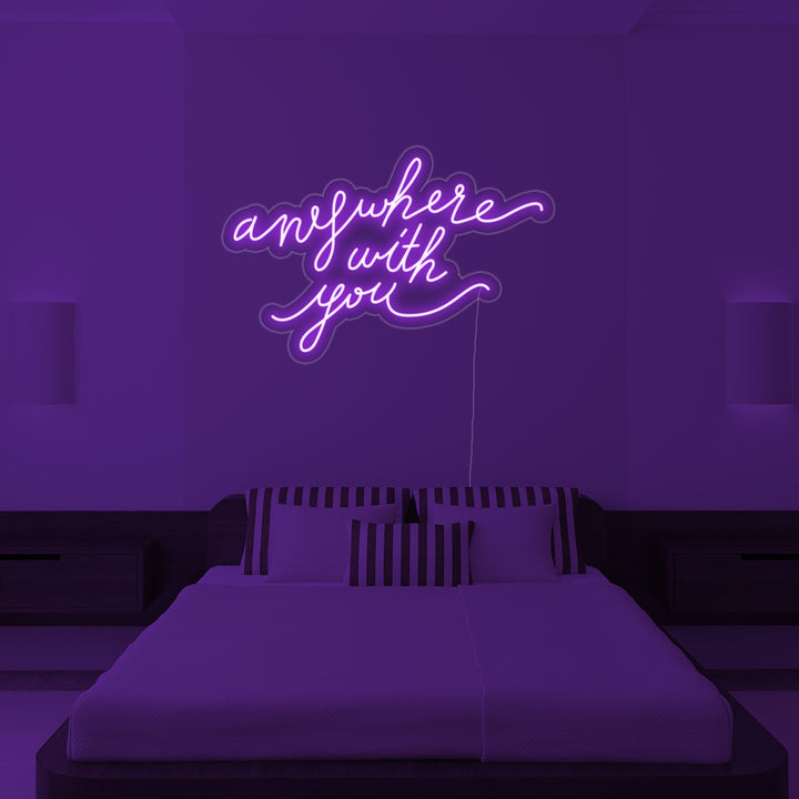 The 'Anywhere With You' neon wall decor sign positioned above a bed in a cozy, stylish bedroom setting, casting a warm ambient light.