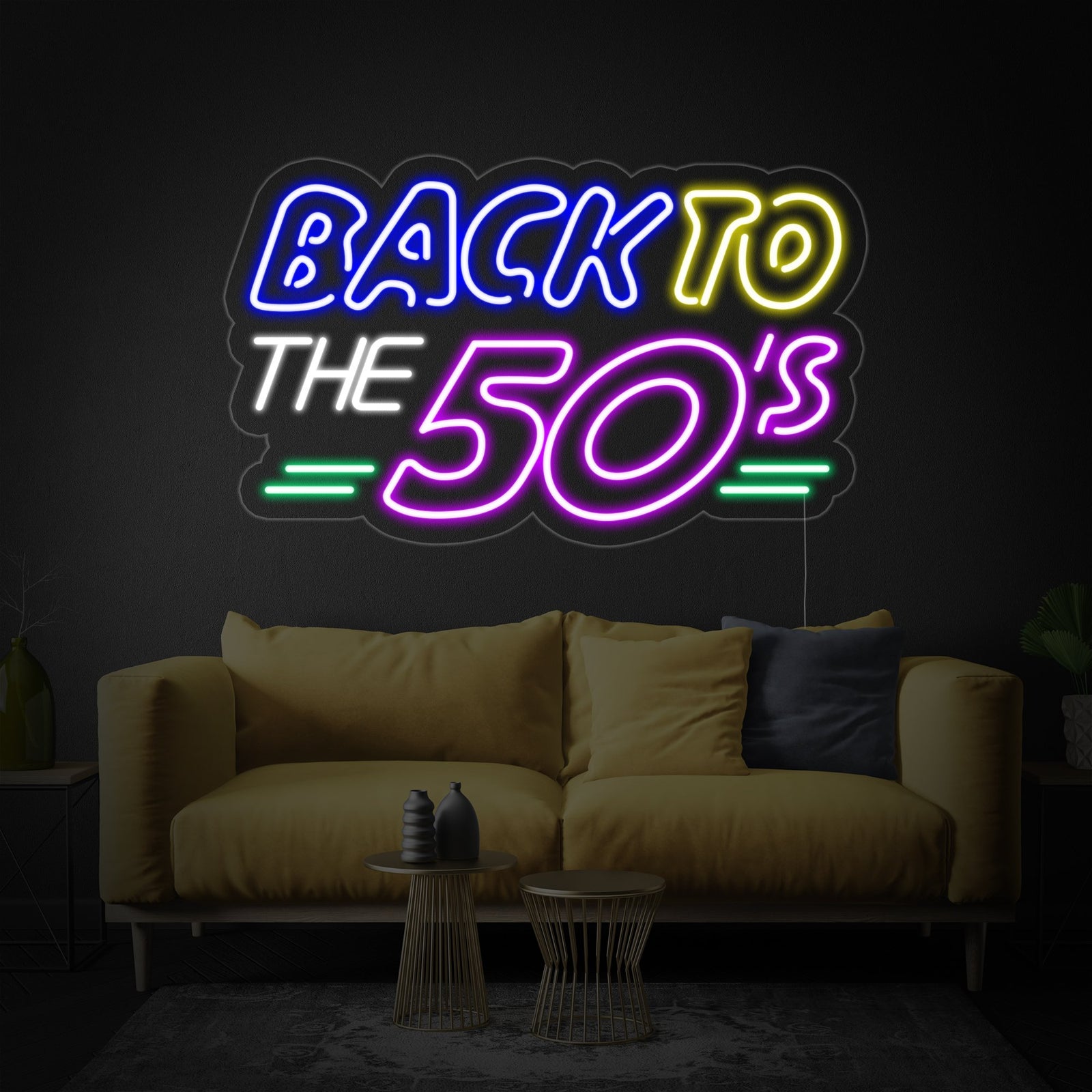 Close-up of the glowing 'Back To The 50s' neon sign on a clear backing, with a blurred classic American diner counter and booth in the background.
