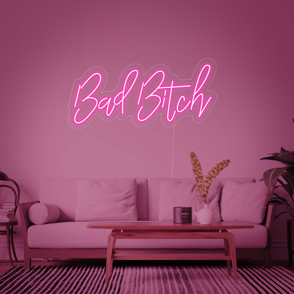 A luminous 'Bad Bitch' neon sign in glowing script lettering, mounted securely to a clear acrylic backing ready for wall installation.