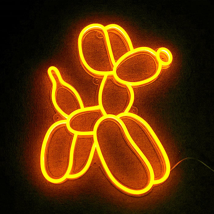 A fabricated neon sign glowing pink, shaped like a playful balloon dog, mounted on a clear acrylic backboard against a light neutral background.