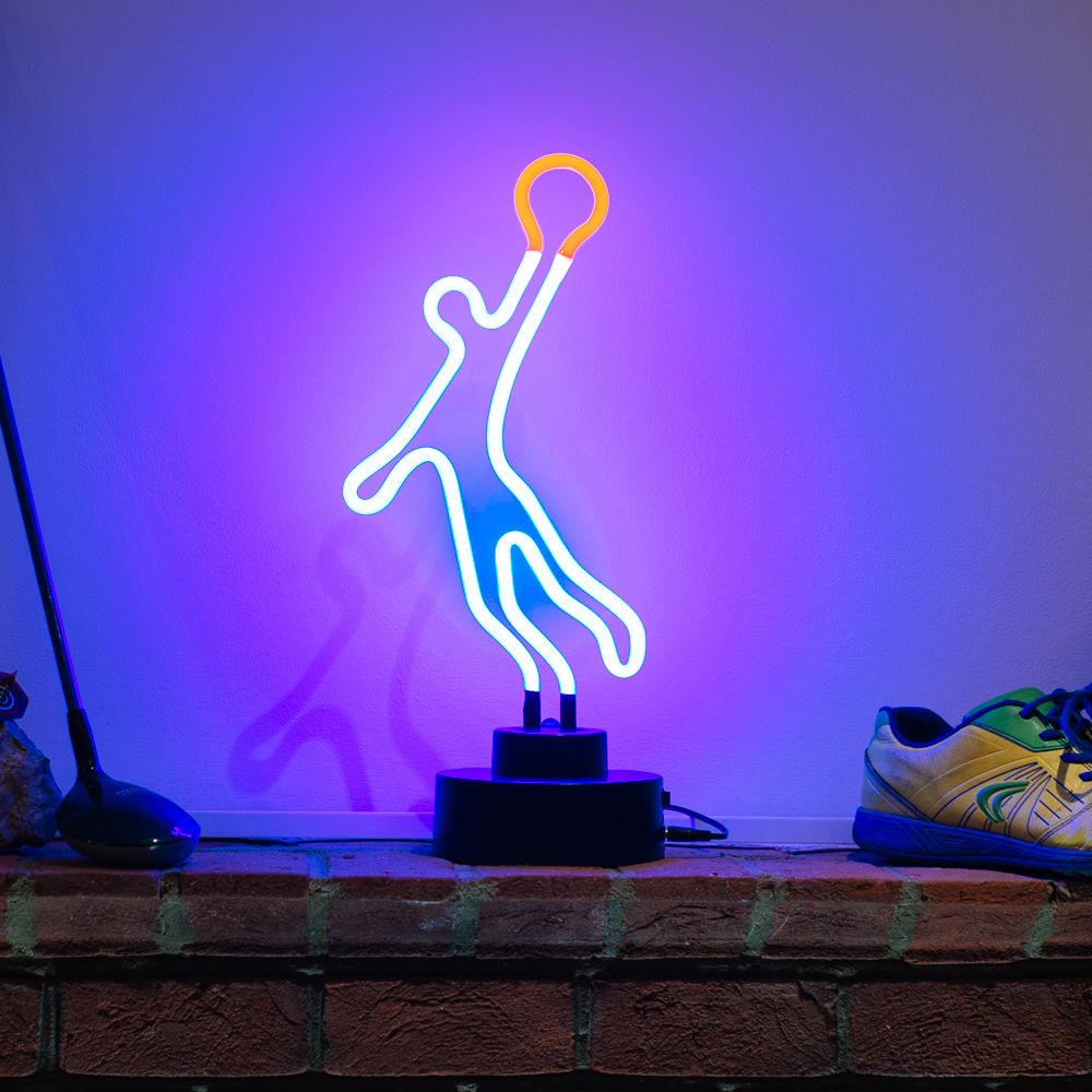 A glowing glass neon table sign depicting an orange and red basketball player figure, displayed against a rustic brick wall.