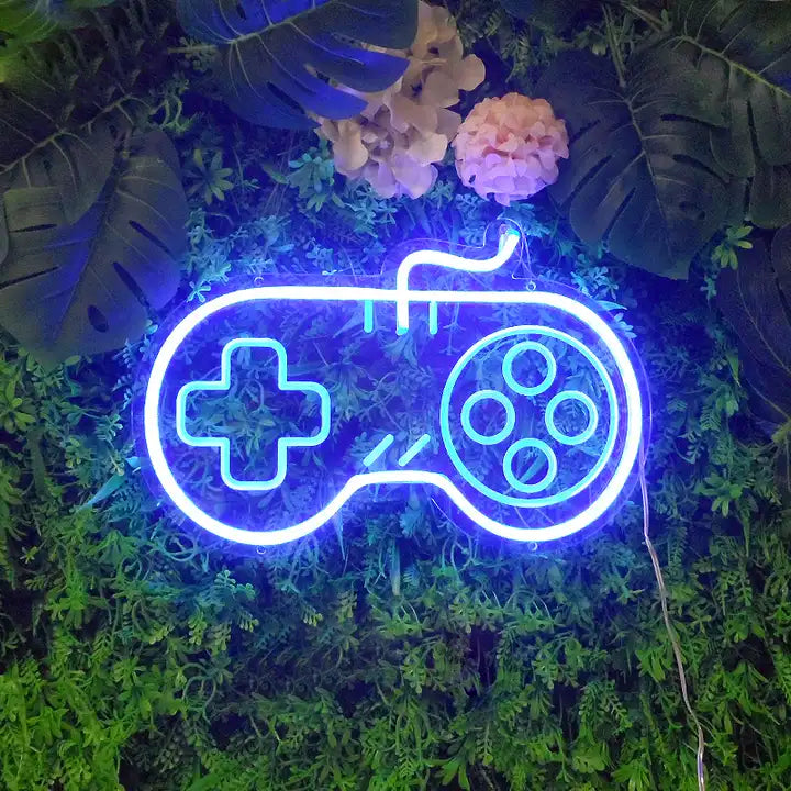 A "Game Controller" mini neon sign glowing brightly on a wall surrounded by artificial plants.