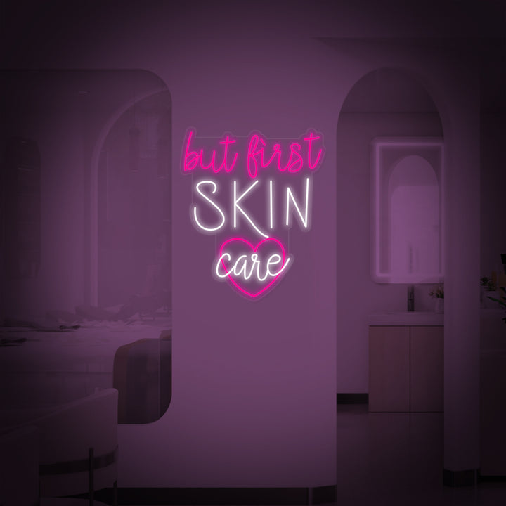 A brightly lit pink 'But First Skin Care' neon wall sign mounted on a clean white surface.