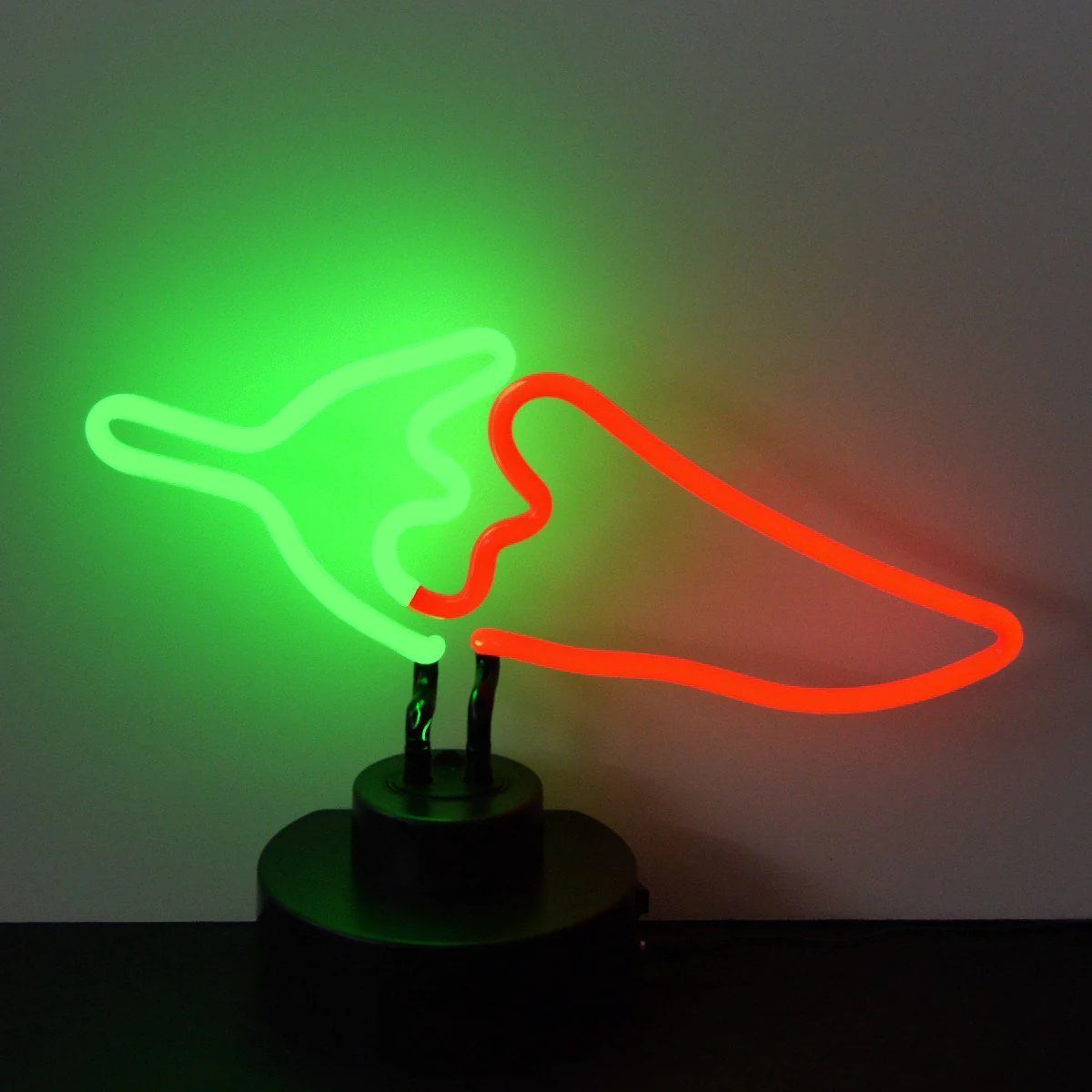 Red chili pepper neon sign glowing brightly on a table base against a wall.