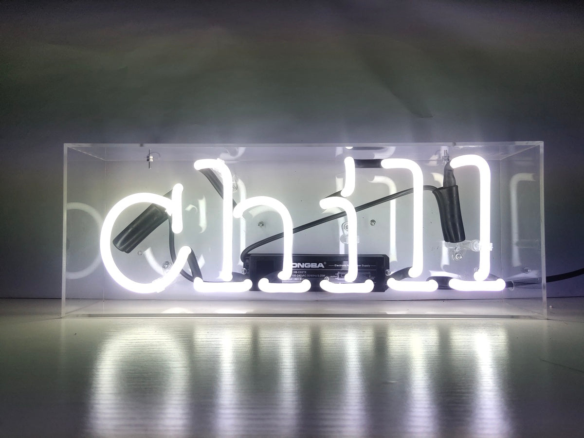 Hand-crafted orange neon sign reading 'Chill' in cursive, glowing inside a clear acrylic display box on a table.